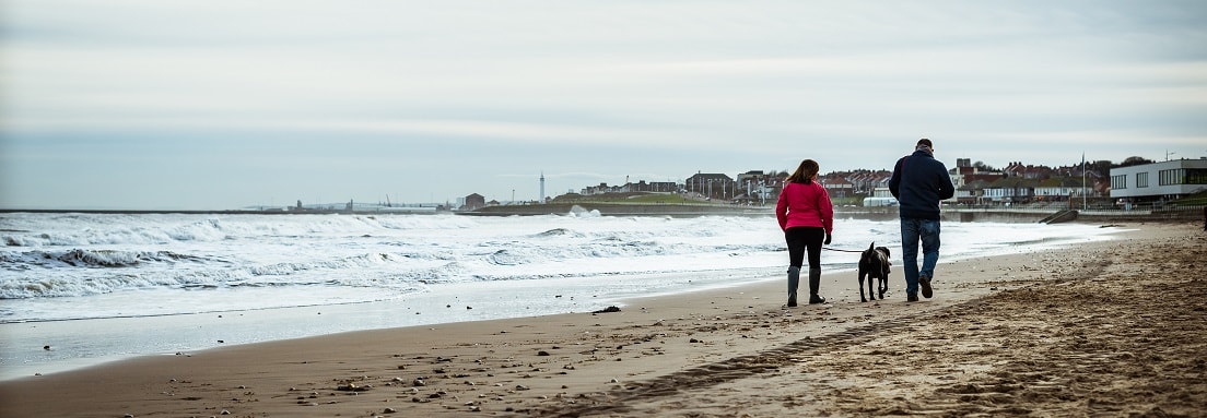 man woman and dog walking on beach 