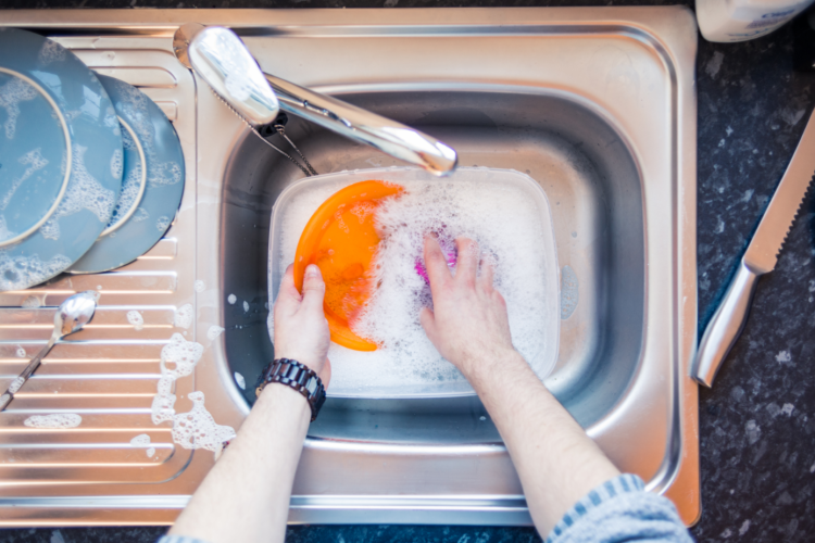 person washing plate in kitchen sink 