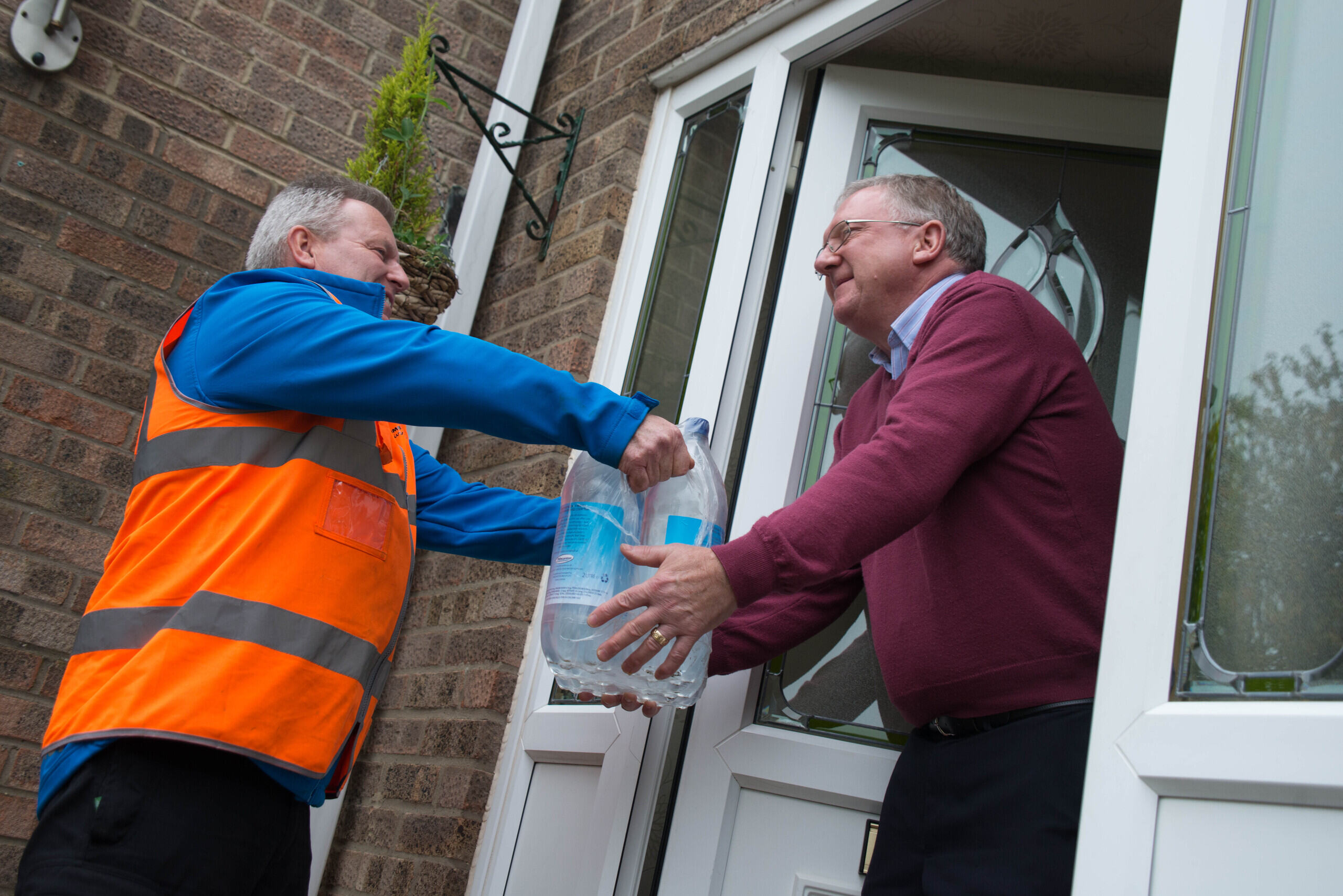 employee providing bottled water to man at front door