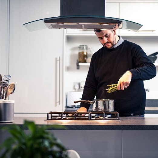 person putting vegetables into pan on hob