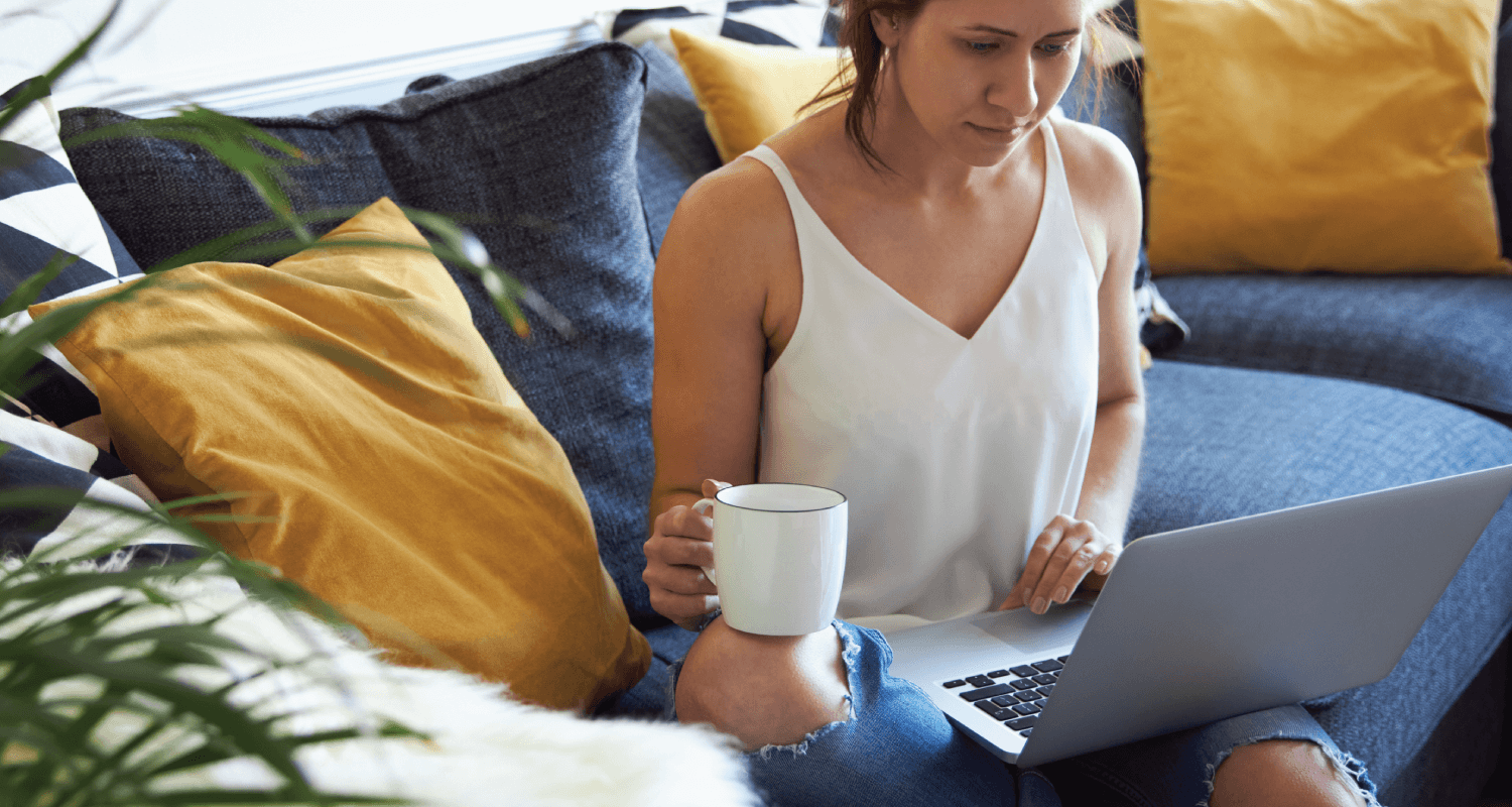 Girl sitting on couch with a cuppa on laptop
