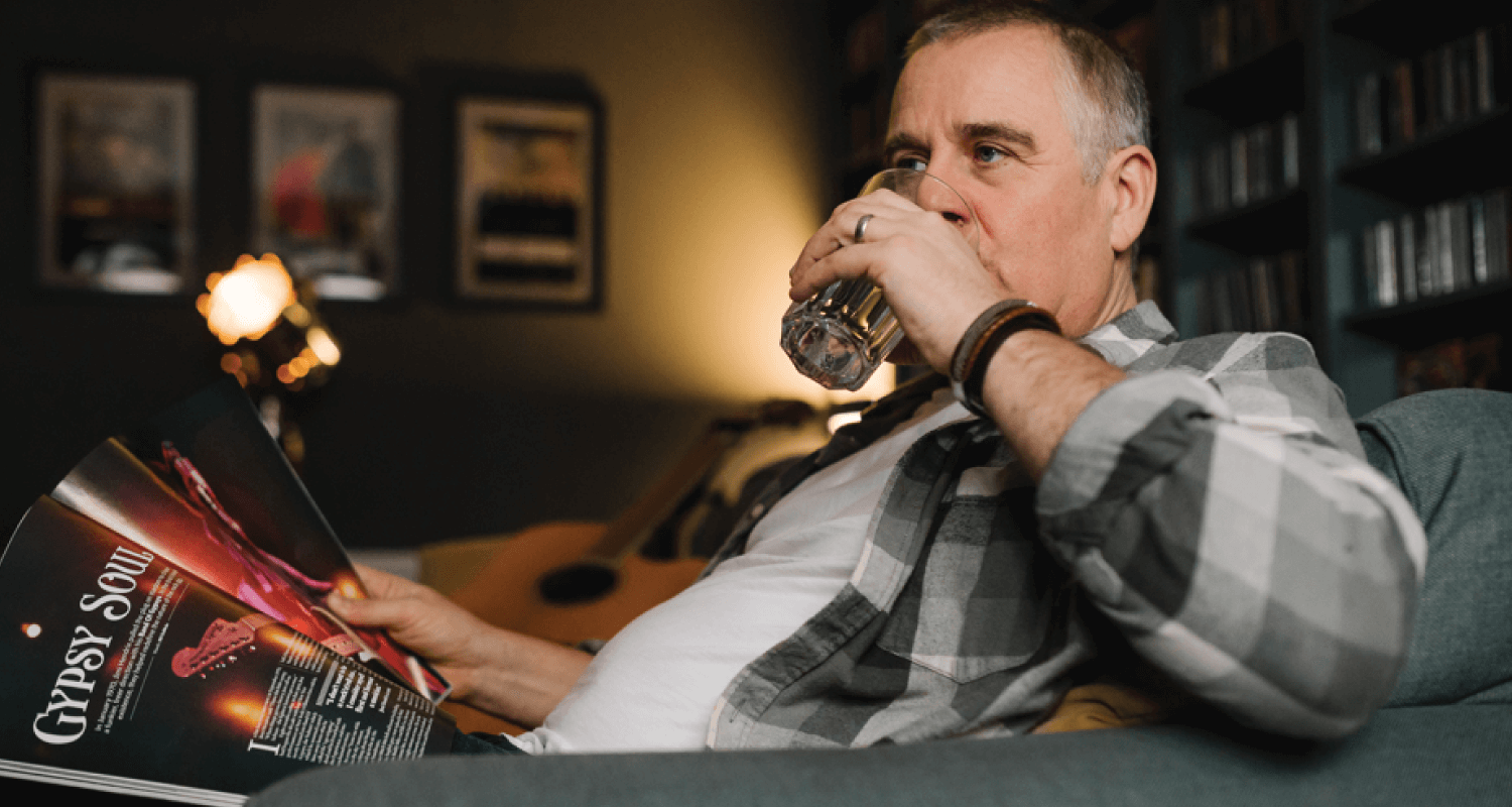 Man on couch reading music magazine drinking a glass of water