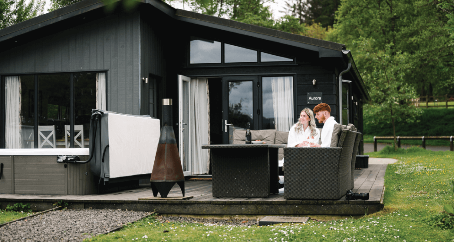 Young couple man and woman sitting outside on garden furniture in front of a Kielder Waterside lodge