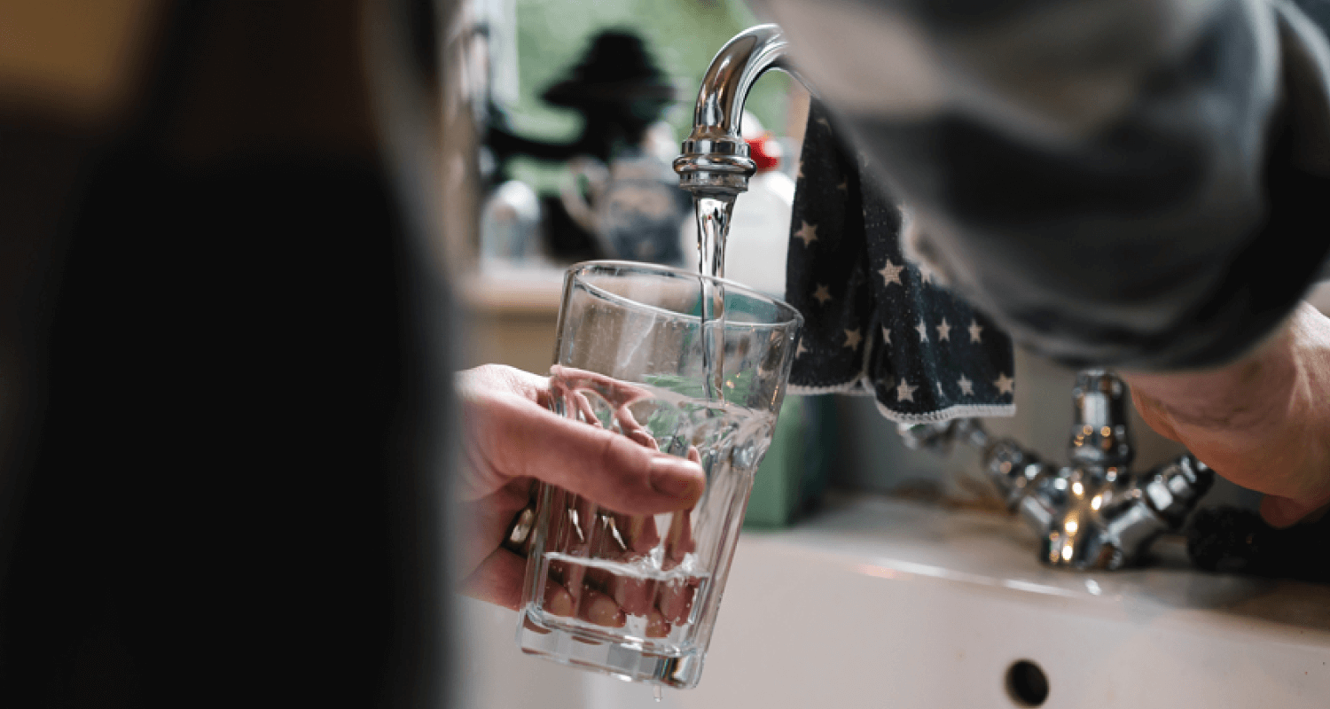 Glass being filled with water from a running tap in kitchen