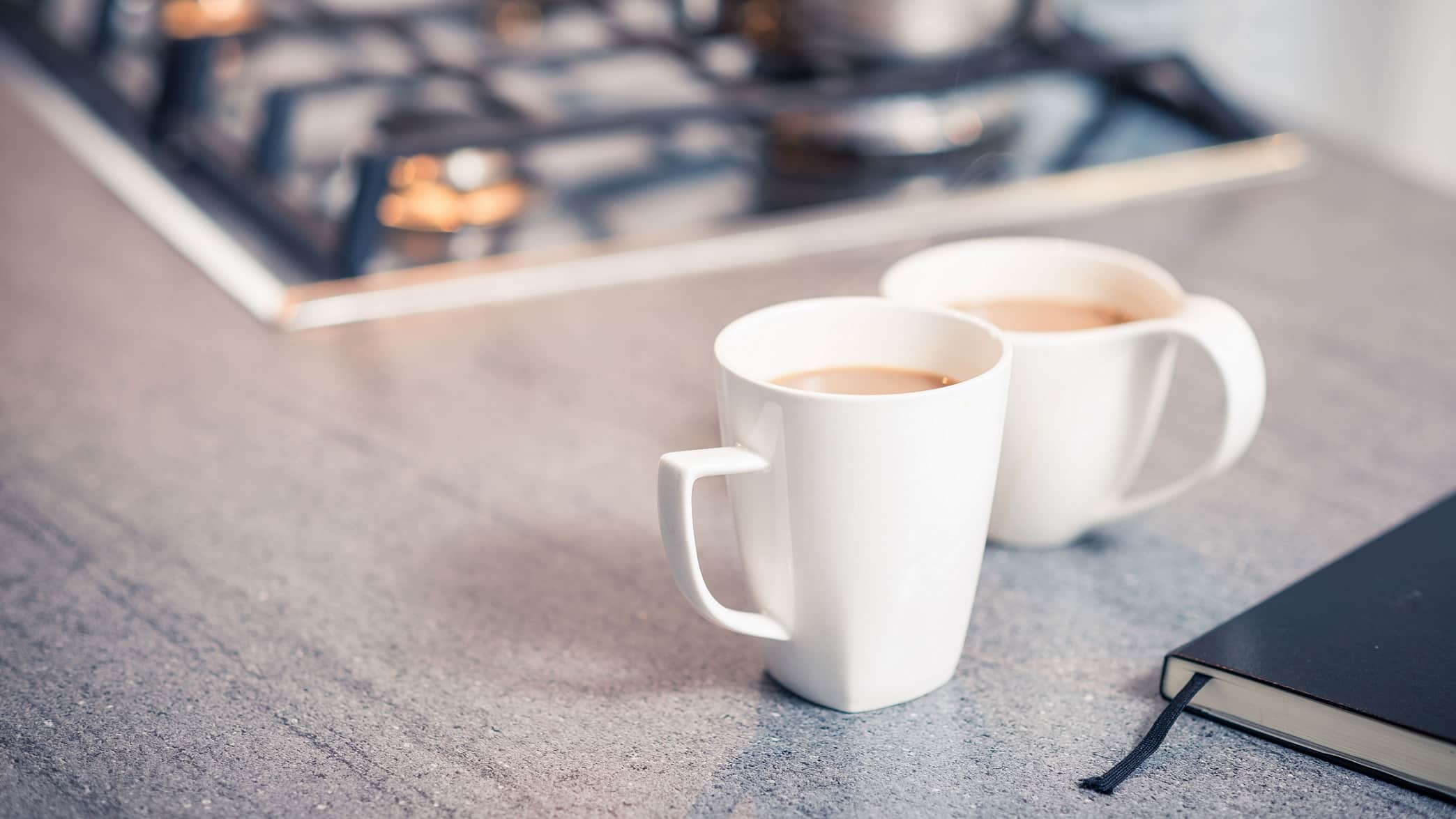Two white mugs of tea on kitchen bench