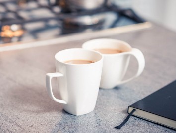Two white mugs of tea on kitchen bench